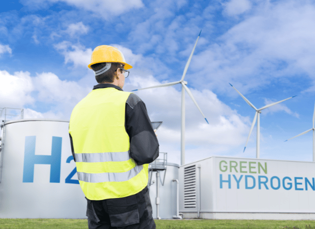 a man in a yellow hard hat and reflective vest standing in front of windmills Stanislav Kondrashov